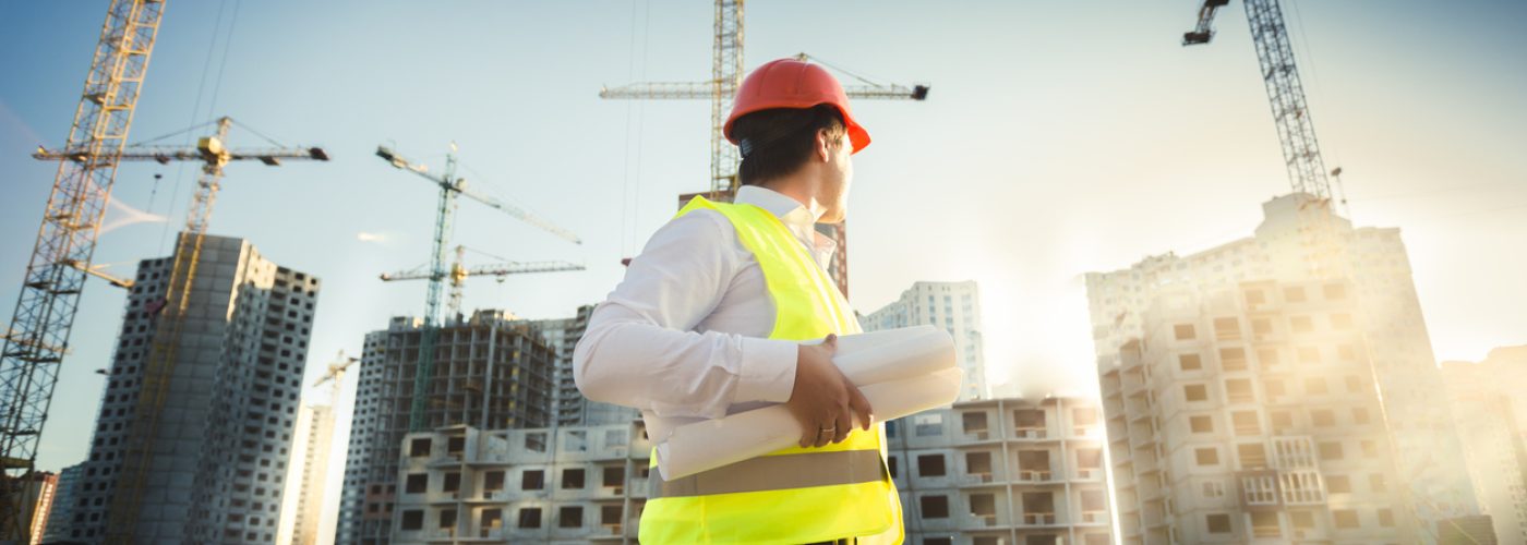 Man in hardhat and green jacket posing on building site